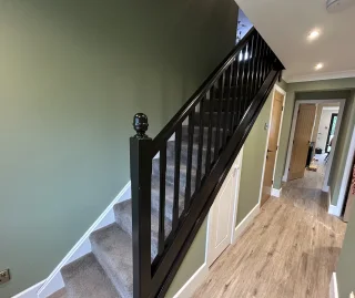 Hallway with green painted walls, black wooden staircase and grey carpeted steps