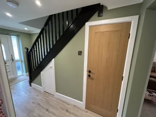 Hallway with green walls, black staircase, oak door and wood flooring